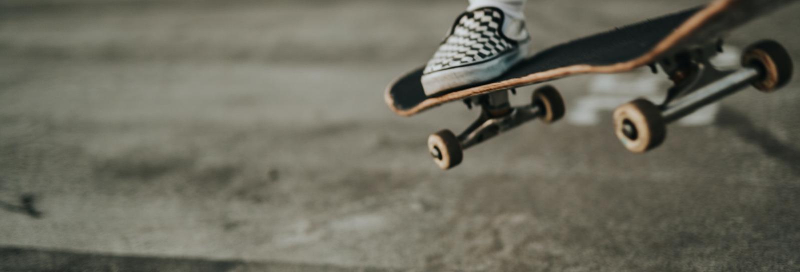 En nærbillede af et skateboard med en fod på, der er ved at lande på jorden