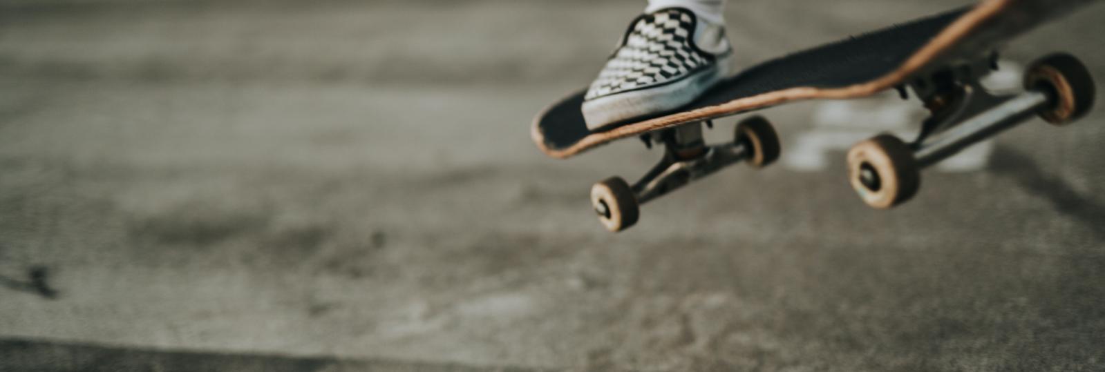 En nærbillede af et skateboard med en fod på, der er ved at lande på jorden